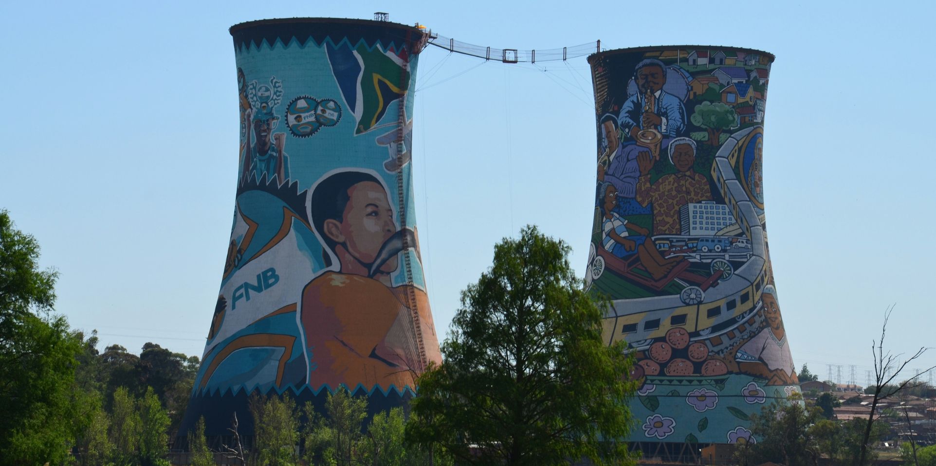 Two old cooling towers in South Africa, no longer used for energy, they are painted with bright imagery of South Africans and South African historical figures.