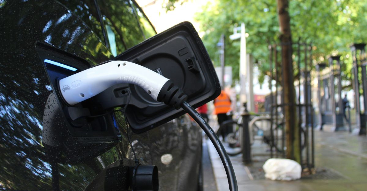 Side view of a black electric car plugged in to a charger.