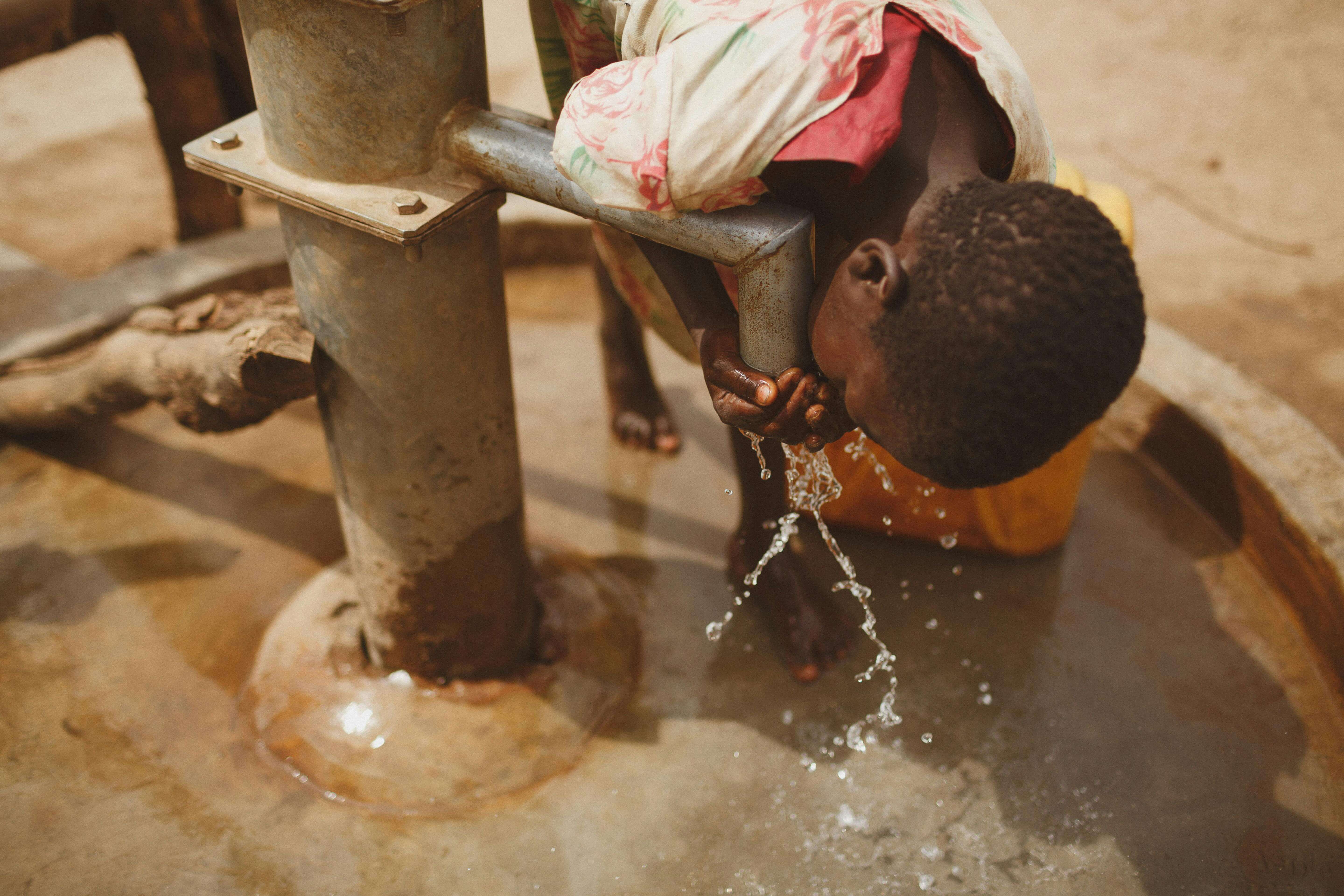 child drinking from a community water pump