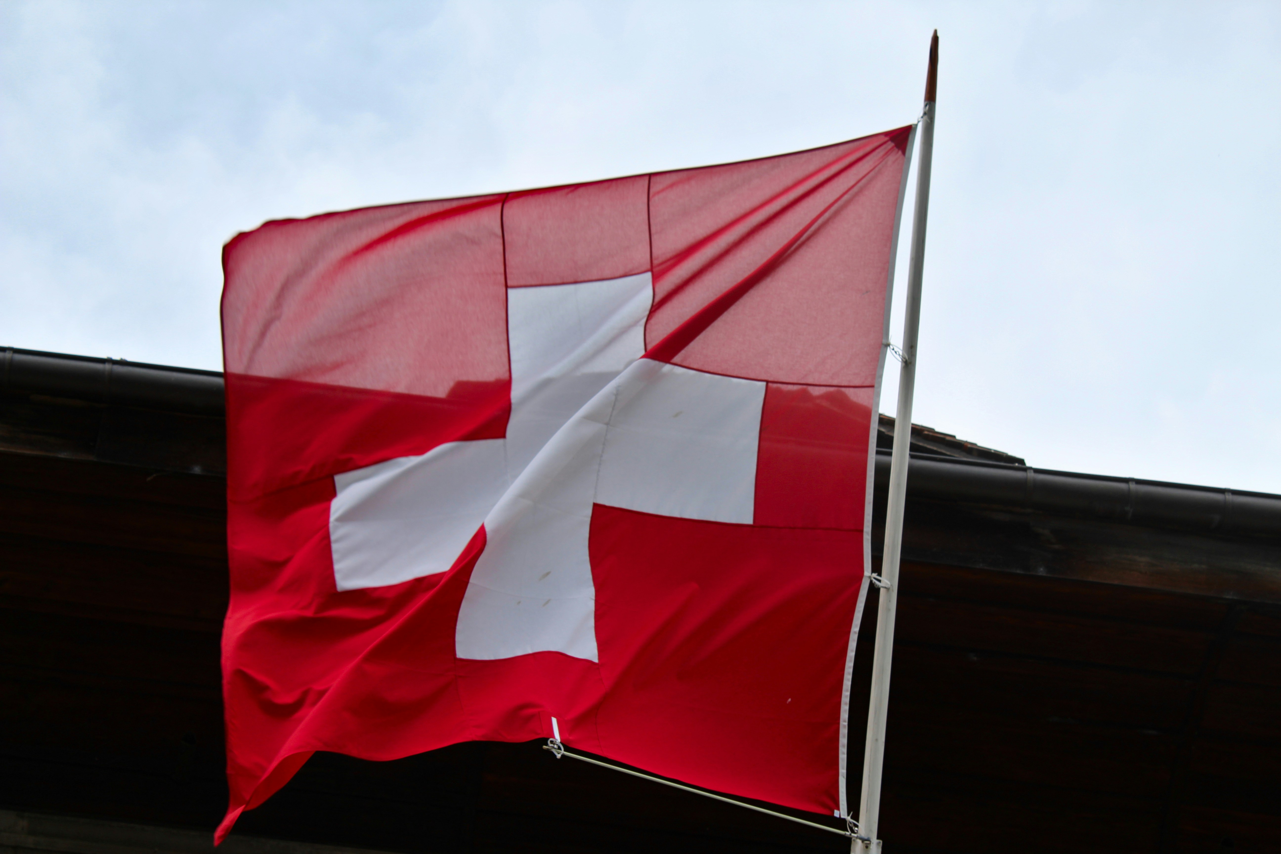 Swiss flag flying against the top of a building and a light, sky background